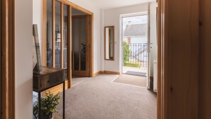 A hallway with a wooden door, a glass door leading outside, and a small table with a plant.