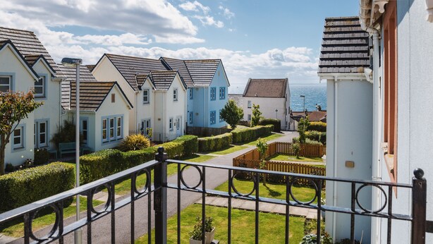 A residential street with houses, a well-maintained lawn, and a clear view of the sea.