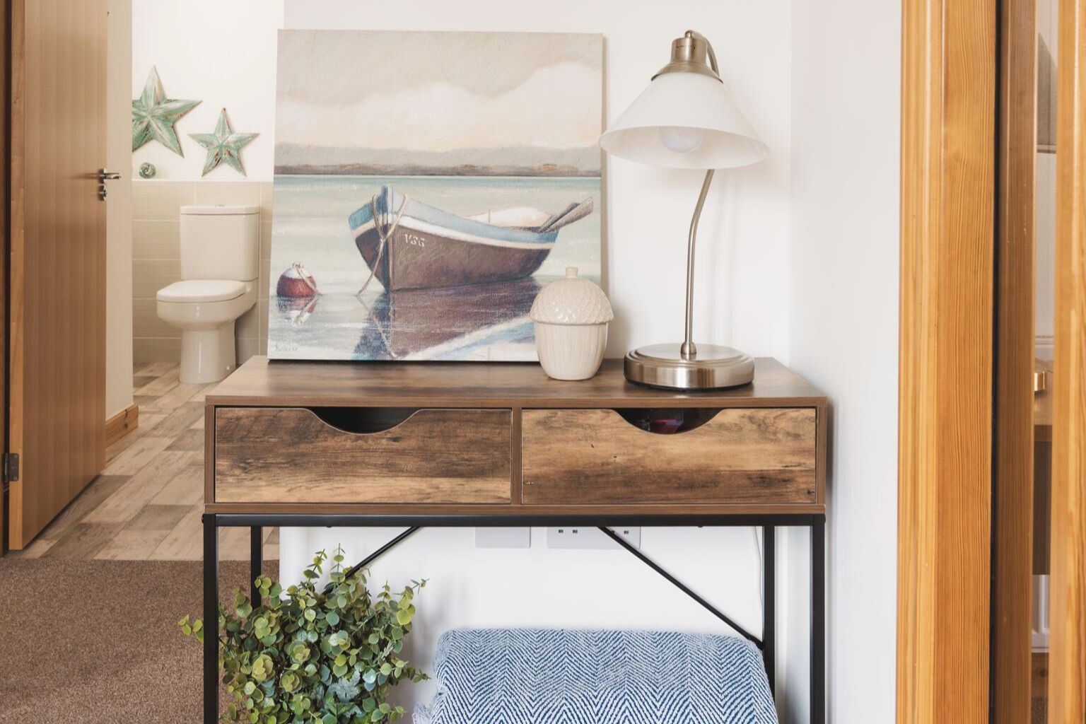 A wooden desk with a lamp, a painting of a boat, and a small plant.
