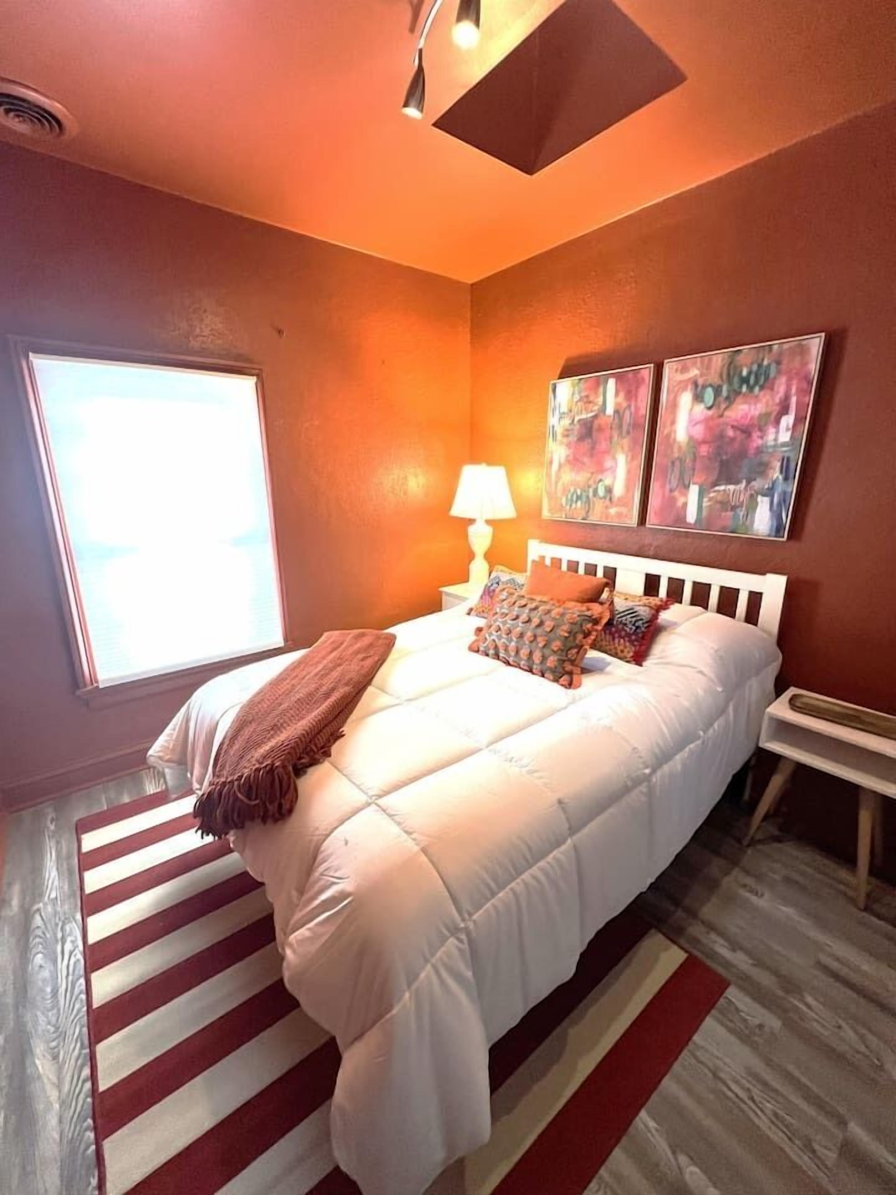 A bedroom with a bed, a nightstand, a lamp, and two paintings on the wall.