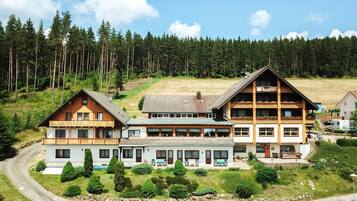 Situated in a forested area, this lodge offers a traditional Alpine-style retreat with a balcony and a winding road leading to its entrance.