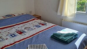 Un dormitorio con cama, ventana con cortinas, radiador y un armario de madera sobre la cama.