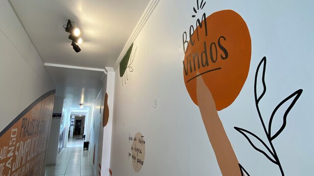 A hallway with a sign reading "Bem vindos" and a plant illustration. - Ok Inn Hotel Tubarão (Tubarao)
