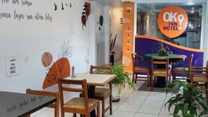 A modern hotel lobby with wooden furniture, a central table with a plant, and a wall with decorative leaf art. - Ok Inn Hotel Tubarão (Tubarao)