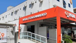 A hotel with a prominent orange and white sign, air conditioning units, and a covered entrance area. - Ok Inn Hotel Tubarão (Tubarao)