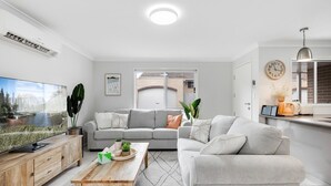 Una sala de estar moderna con un sofá gris, una mesa de centro de madera y un televisor sobre un mueble de madera.