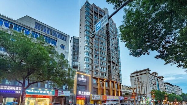 A multi-story building with commercial shops on the ground floor, a prominent sign indicating a hotel, and a parking area in front. - Core Clould of hotel (Nanchang County)