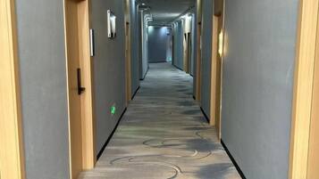Un couloir d’hôtel avec un sol recouvert de moquette, des portes de chaque côté et un éclairage au plafond.