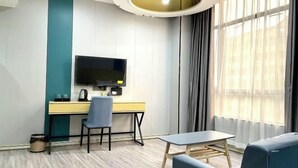 A modern hotel room with a wooden floor, a desk with a flat-screen TV, a blue chair, a small table, and a large window with curtains. - Core Clould of hotel (Nanchang County)