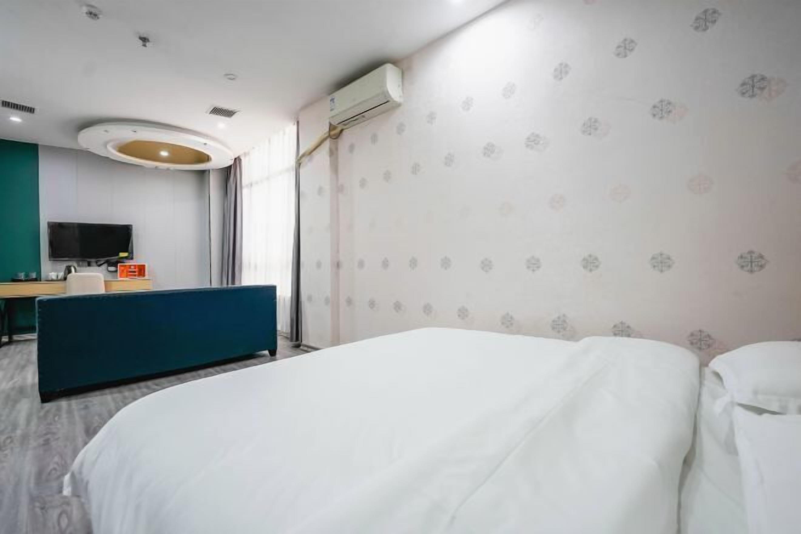 A hotel room with a bed, a desk, a TV, and an air conditioning unit.