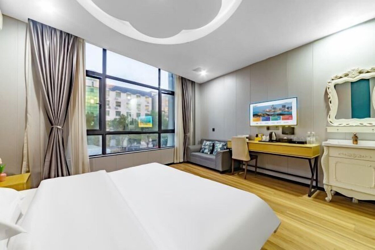 Habitación de hotel con una cama grande, un escritorio con computadora, un televisor y vista a edificios desde la ventana.