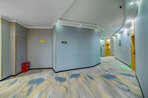A hotel corridor with a curved ceiling, a red trash bin, and directional signs. - Core Clould of hotel (Nanchang County)