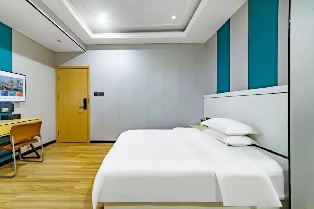 Habitación de hotel con cama, escritorio, silla, piso de madera y una puerta.