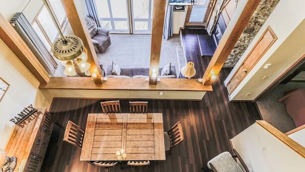 A spacious dining area with a wooden table and chairs, a chandelier, and a view of a living room with a sofa and a television. - Ski-In/Ski-Out Mountain Retreat with Pool and Private Indoor Hot Tub (Granby)