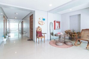 Un pasillo amplio con una puerta de madera al final, una zona de estar con una mesa redonda y sillas, y una obra de arte colgada en la pared.