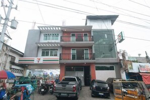 A multi-story building with a 7-Eleven convenience store on the ground floor, a balcony on the second floor, and a parked truck in front. - Budget Backpackers Transient House Near Naia by RedDoorz (Pasay)