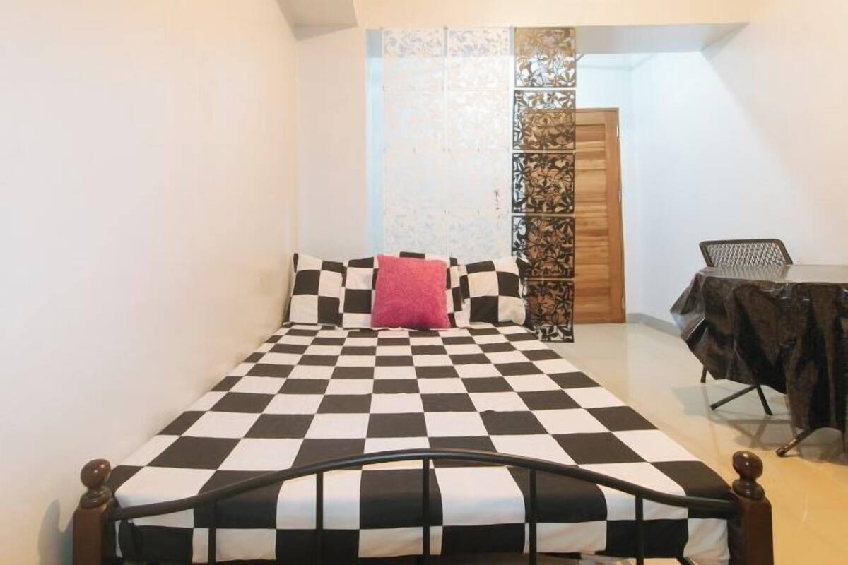 Ein Schlafzimmer mit kariertem Bettbezug, einem Holzkopfteil, einem Schreibtisch mit Stuhl und einem dekorativen Raumteiler.