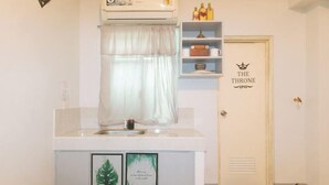 A small kitchenette with a sink, a window with a white curtain, a shelf with bottles, and a door with a crown symbol and the words "THE THRONE". - Budget Backpackers Transient House Near Naia by RedDoorz (Pasay)