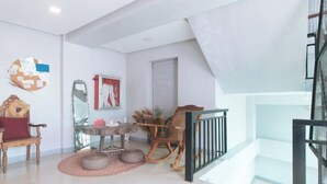 A modern living room with a wooden rocking chair, a round table, and a red cushion. - Budget Backpackers Transient House Near Naia by RedDoorz (Pasay)