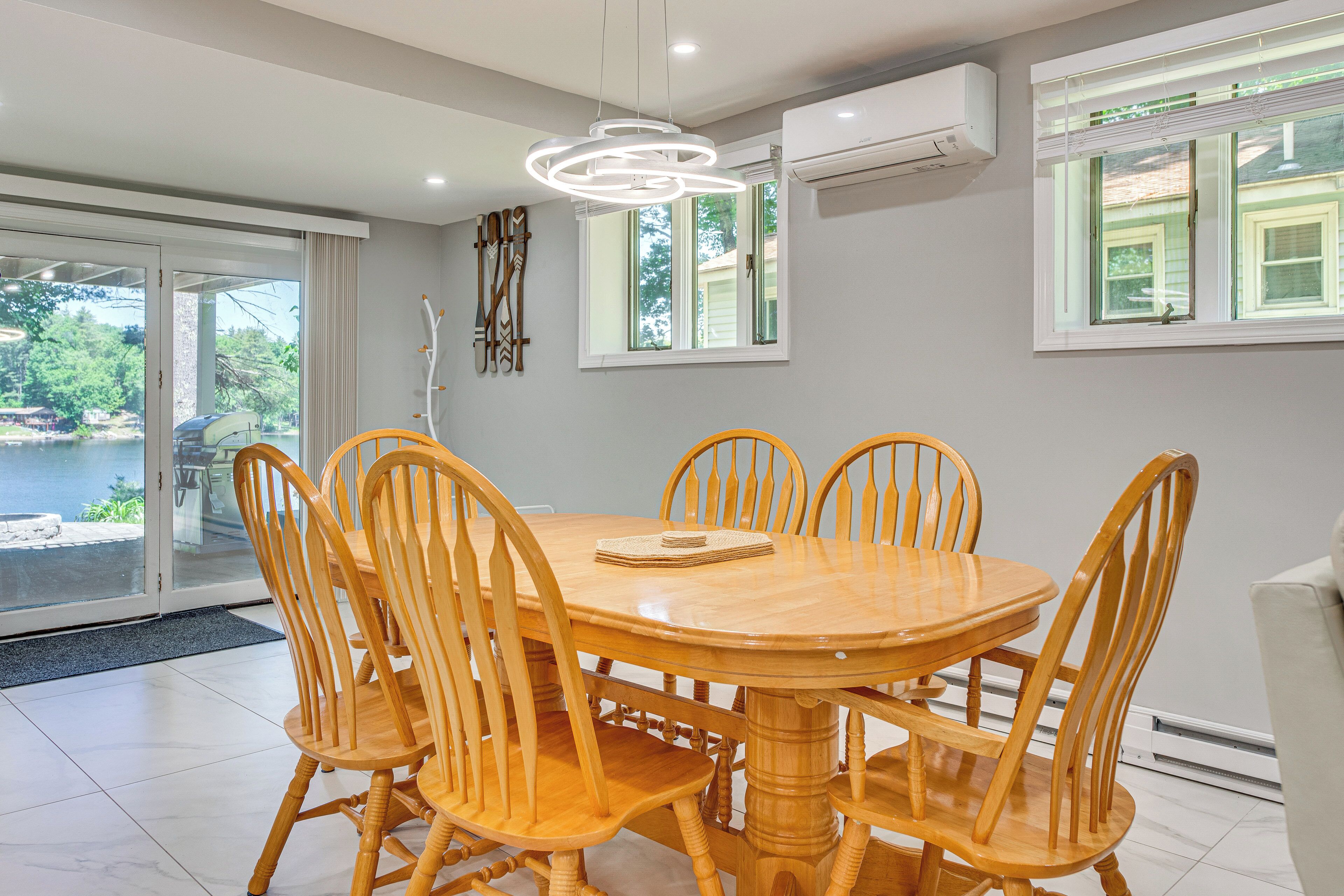 A dining area with a round wooden table and chairs, a modern pendant light, and a view through glass doors.