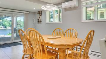 A dining area with a round wooden table and chairs, a modern pendant light, and a view through glass doors.