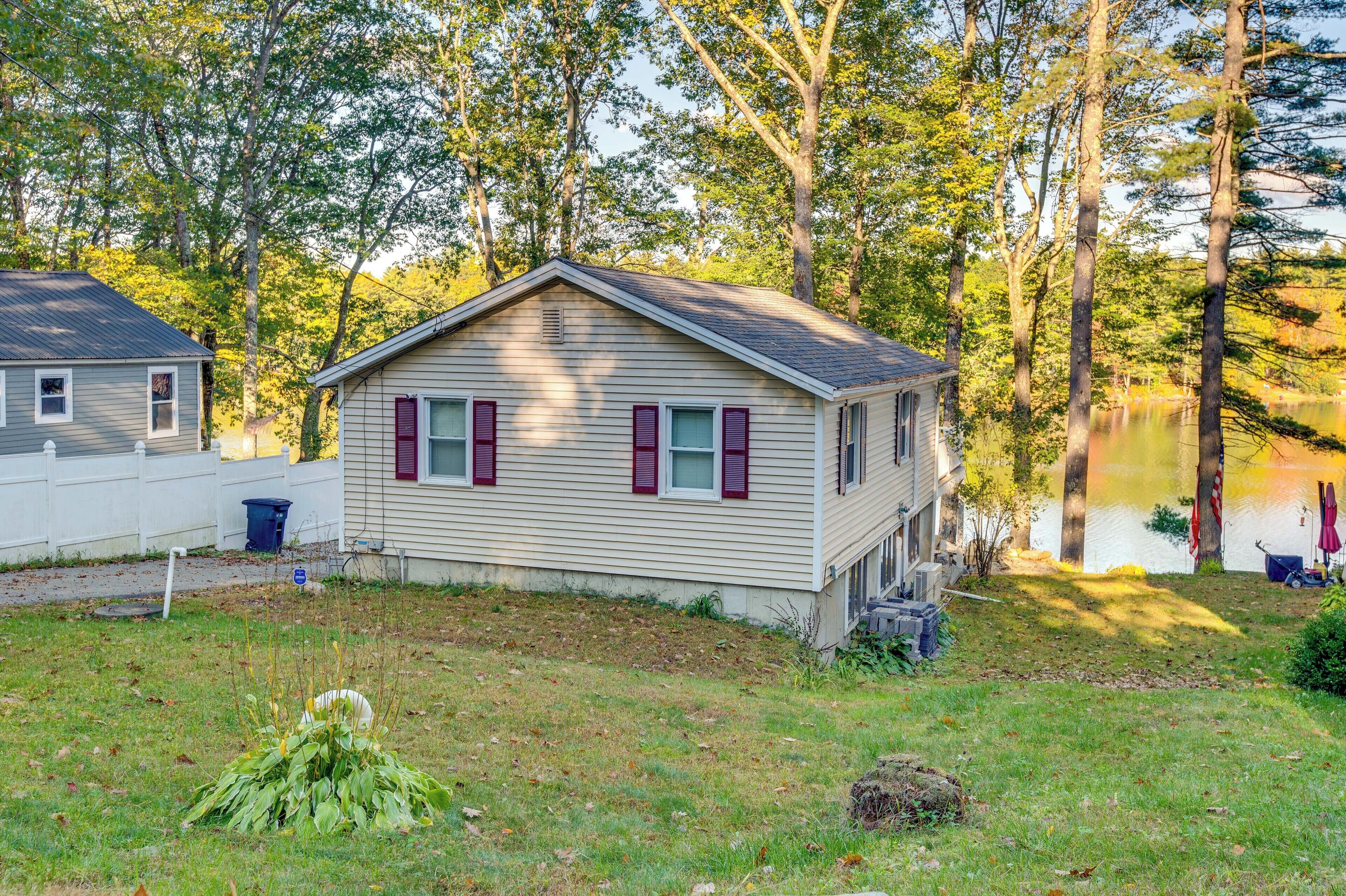A small, single-story cabin with a gabled roof, a front porch, and a view of a lake.