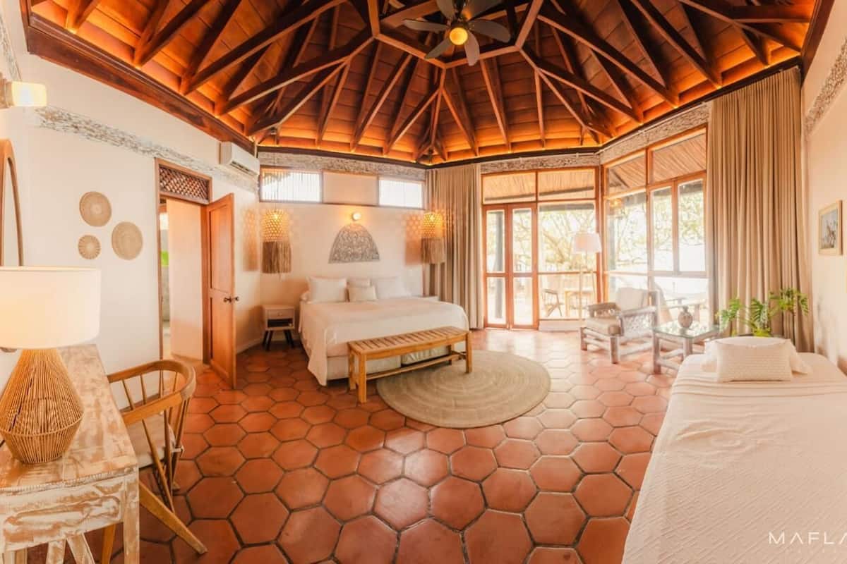A spacious bedroom with a large bed, a wooden ceiling, and a view of the outdoors.