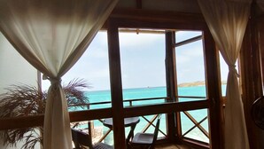 A room with a view of the ocean through large windows, wooden flooring, and a small table with chairs. - Rosario Ecohotel  (Rosario Islands)