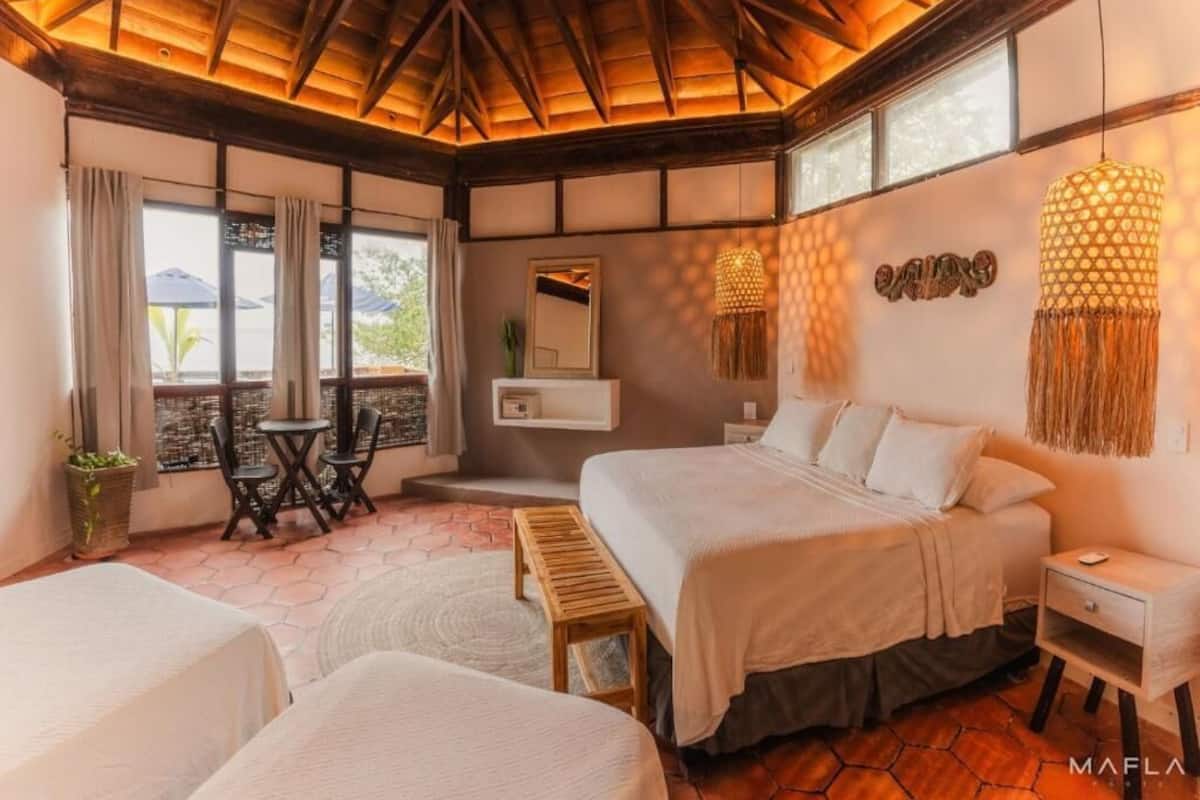 A bedroom with a large bed, a bedside table, a small table with chairs, and a window with curtains.