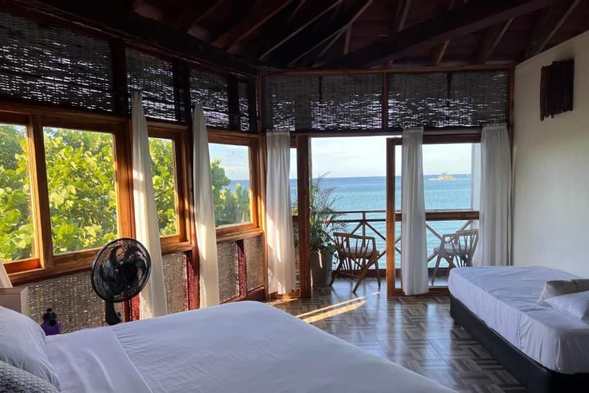 A room with two beds, a fan, and a view of the ocean.