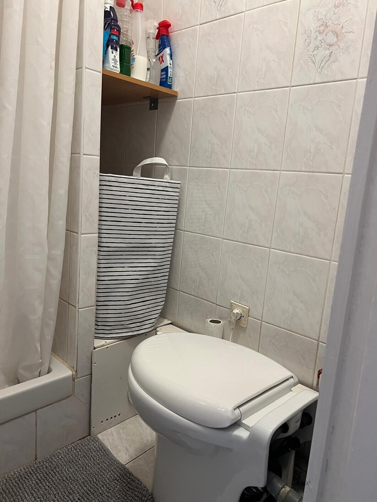Un baño pequeño con un inodoro, una cortina de ducha a rayas y un estante con productos de limpieza.