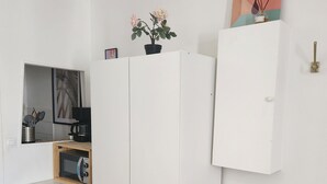 A compact kitchen with white cabinetry, a microwave, and a small wooden shelf.