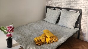 A neatly made bed with patterned bedding, a small table with a vase of flowers, and a brick-patterned wall.