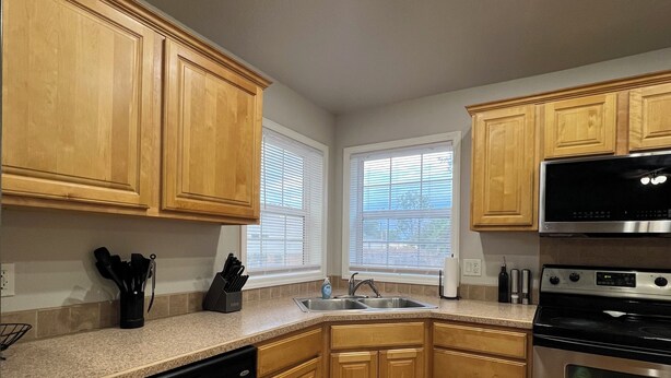Una cocina moderna con armarios de madera, electrodomésticos de acero inoxidable, lavavajillas y encimera negra.