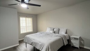 Un dormitorio con cama, mesita de noche, ventilador de techo y ventana con persianas.