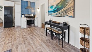 A modern kitchen with white cabinets, a blue backsplash, and a large wave painting on the wall. - Casa Italiana - Charming Home in Little Italy (San Diego)