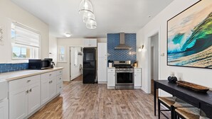 A modern kitchen with white cabinets, a black countertop, and a blue backsplash. - Casa Italiana - Charming Home in Little Italy (San Diego)