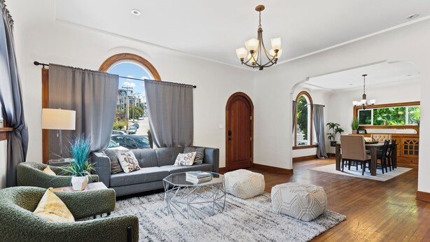 A spacious living room with a grey sofa, green armchairs, a coffee table, and a chandelier. - Casa Italiana - Charming Home in Little Italy (San Diego)