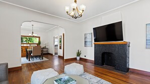 A spacious living room with hardwood floors, a fireplace, a television mounted on the wall, and a dining area visible through an archway. - Casa Italiana - Charming Home in Little Italy (San Diego)