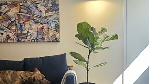 Ein gemütliches Wohnzimmer mit einem blauen Sofa, einem großen abstrakten Gemälde, einem Topf mit Pflanze, einer Trommel und einem gemusterten Teppich.