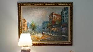Une commode en bois avec des tiroirs, une lampe posée sur le dessus et un tableau encadré accroché au mur.