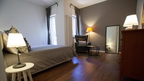 Une chambre d’hôtel avec un lit, une chaise, une petite table, une lampe et un miroir.