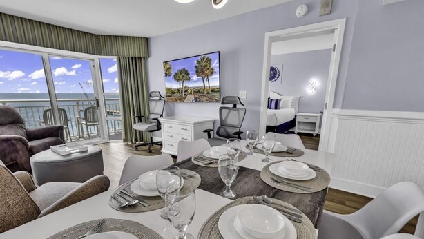 Un coin repas avec une table dressée pour quatre personnes, un canapé et un balcon offrant une vue sur la mer.