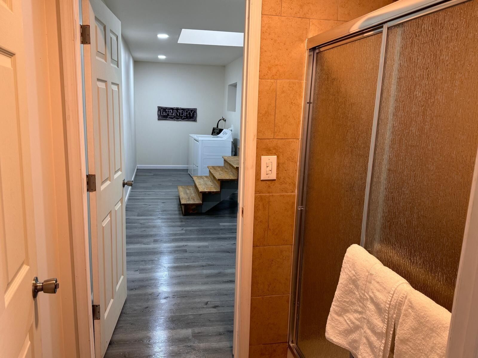 Un couloir avec un plancher en bois, un mur blanc orné d’un panneau indiquant une buanderie, une armoire blanche et une serviette accrochée à une porte.