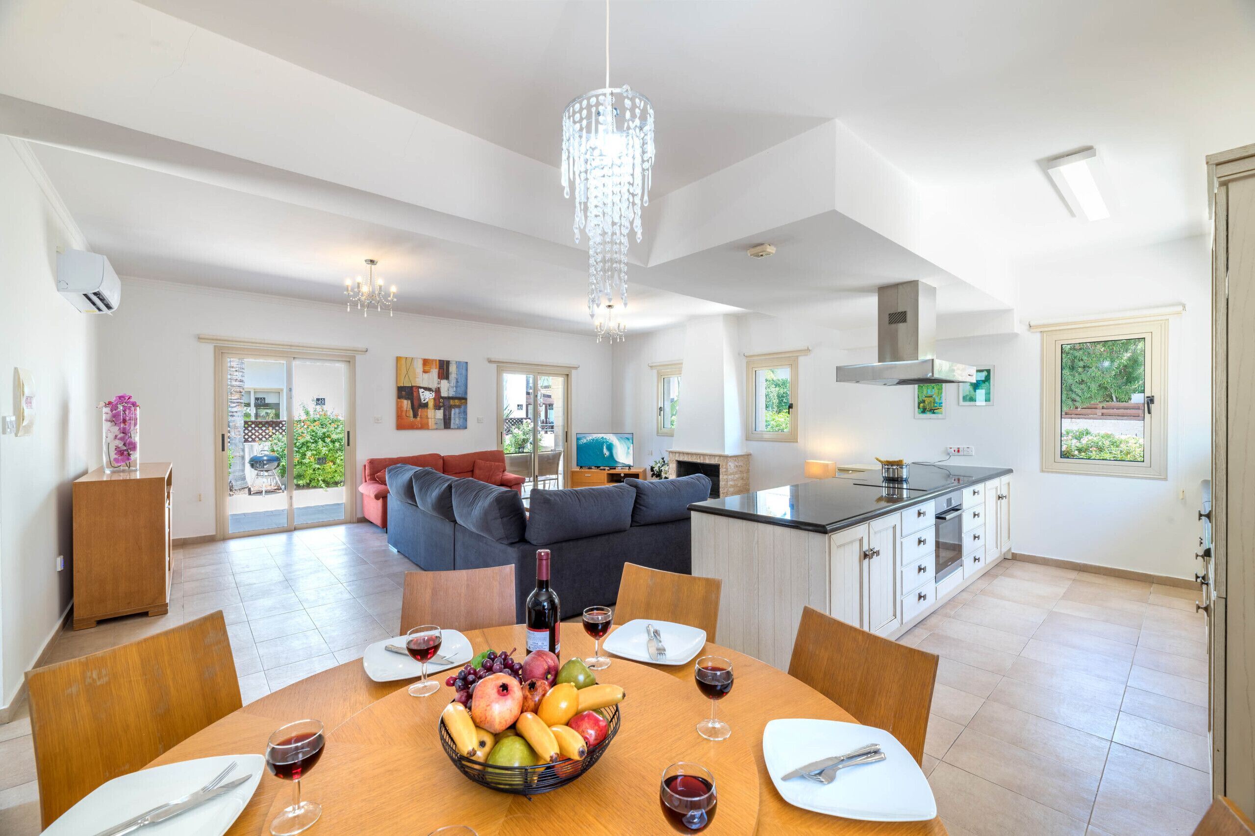 A spacious living area with a dining table set for a meal, a kitchen with modern appliances, and a large chandelier.