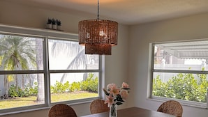 Un comedor con una mesa de madera oscura, sillas de mimbre, una lámpara colgante tejida y un florero con flores.