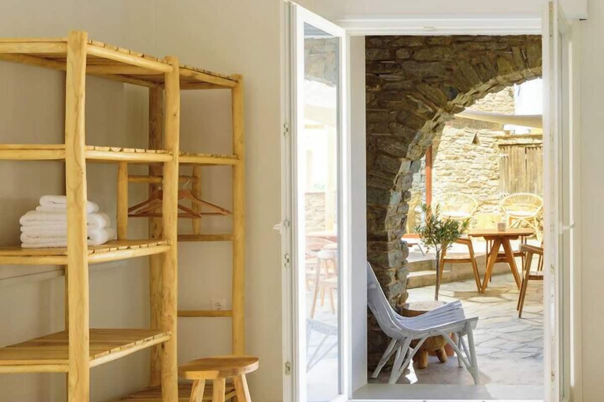 Une chambre avec un lit, une étagère en bois et une vue sur une terrasse extérieure avec des chaises et un mur en pierre.