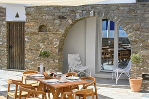 An outdoor dining area with stone walls, wooden tables, and white chairs. - ALASI NEW Hotel - Private Jacuzzi Suites (Tinos)