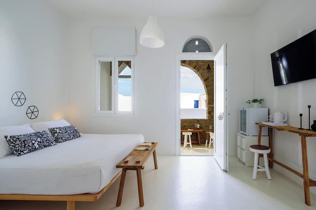 Une chambre à coucher comprenant un lit, des tables de chevet, un téléviseur et donnant sur un espace extérieur aménagé avec une table et des chaises.
