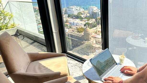 A modern room with a large window overlooking a cityscape, a laptop on a small table, and a cushioned chair. - Redibuk - Beautiful apart 2 BR Barranco (Lima)